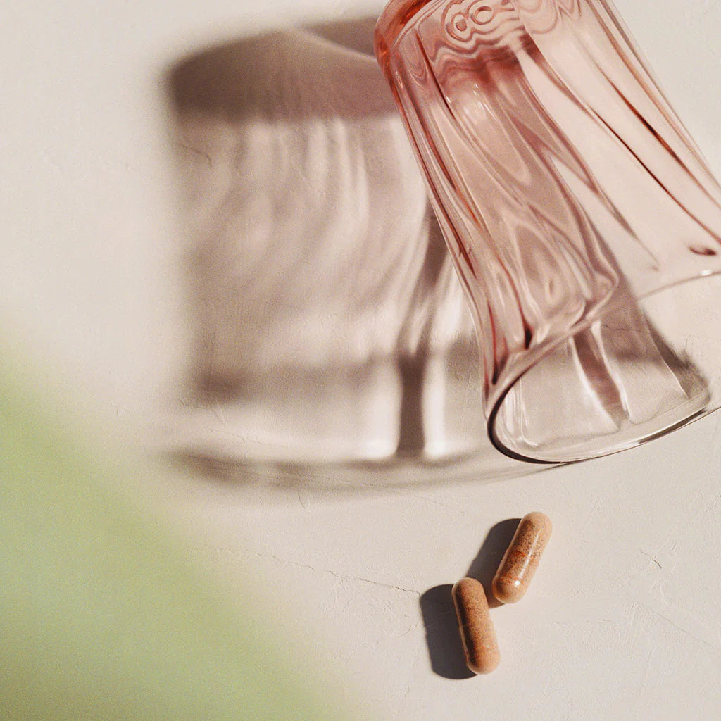 Two capsules next to pink glass