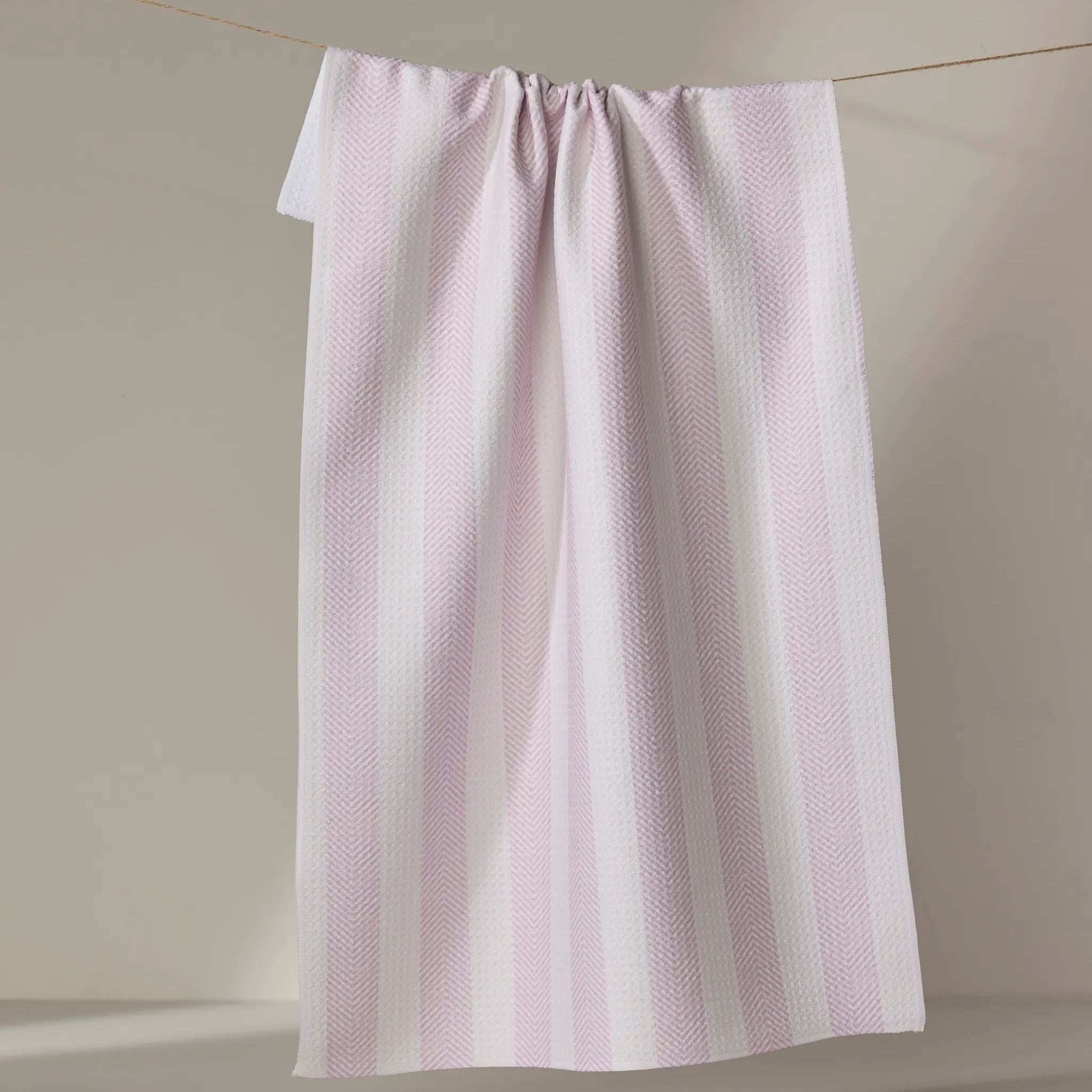 Pink towel with white stripes hanging on a line against a beige wall.