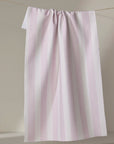 Pink towel with white stripes hanging on a line against a beige wall.
