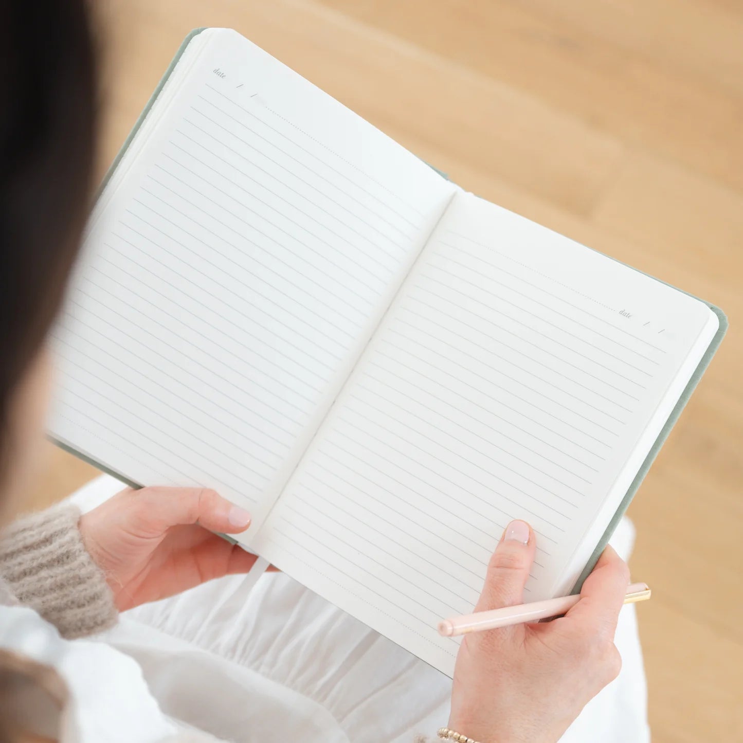 Person holding a notebook with a pen on a wooden surface