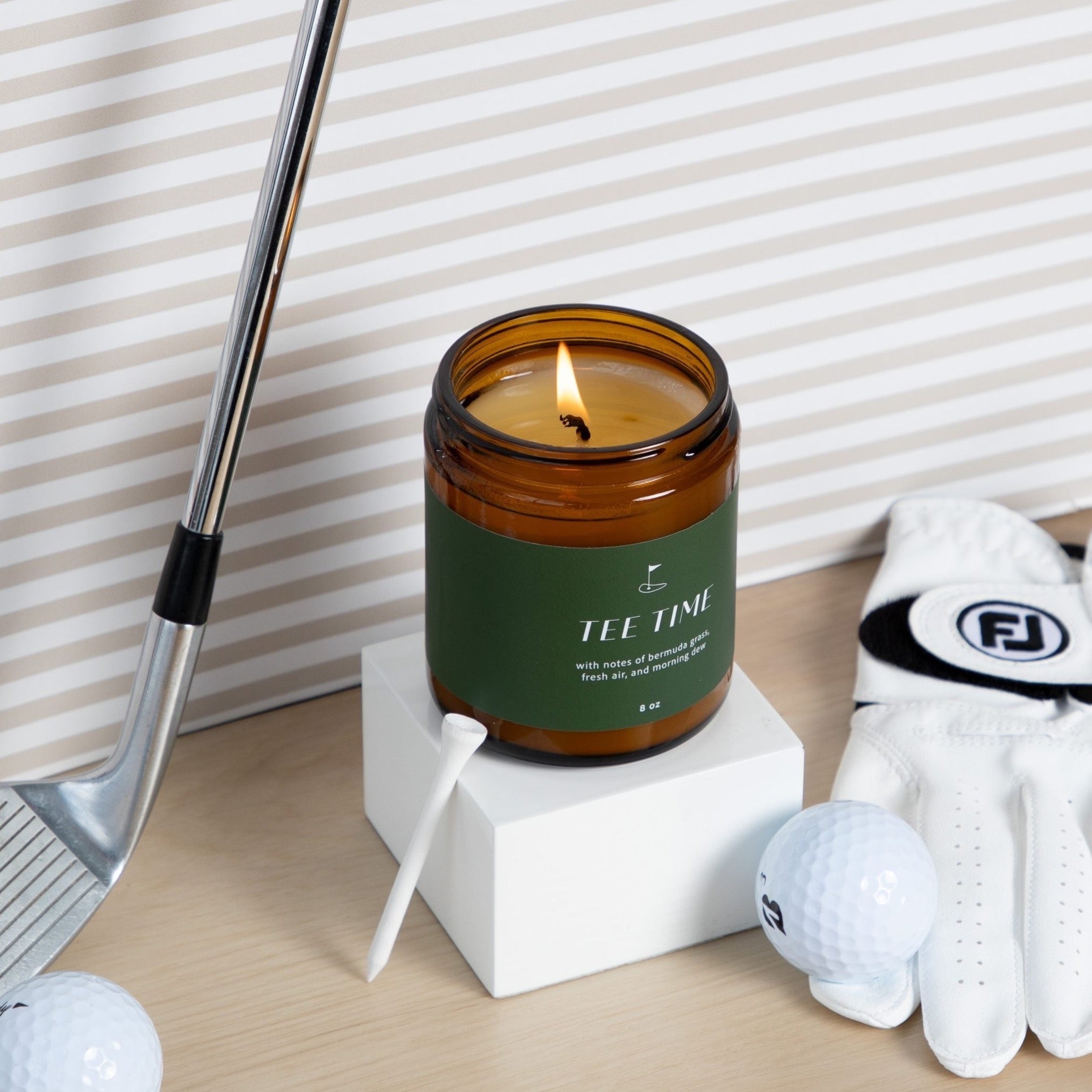 Tea Time Candle on white pedestal with golf equipment around it