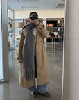 Person wearing a beige trench coat and gray scarf in a room with a mirror.