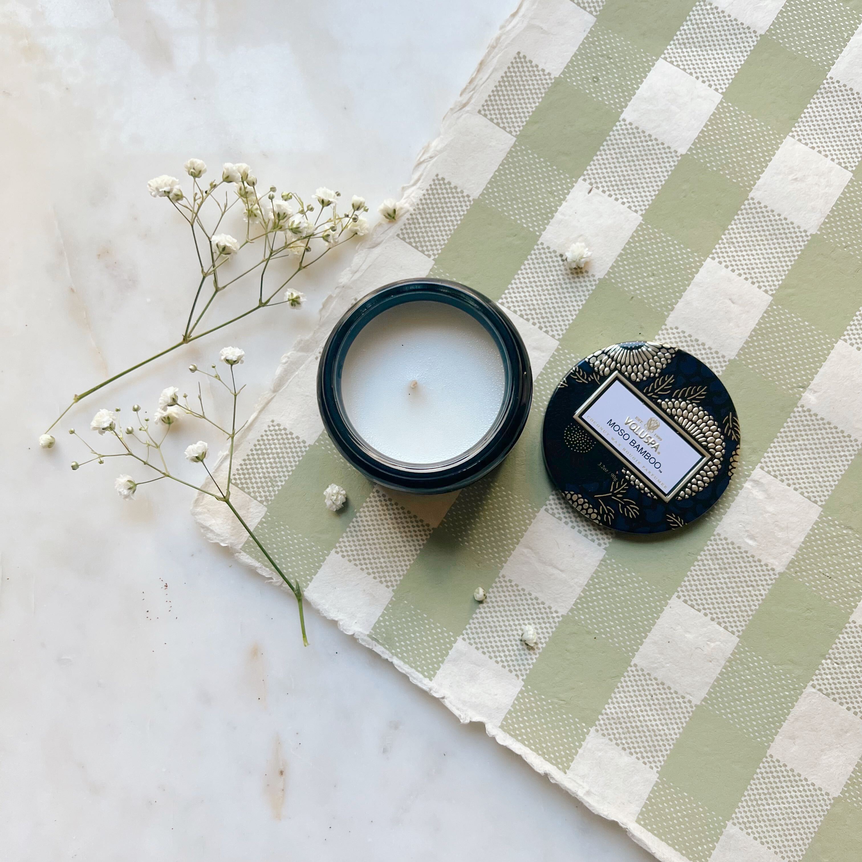 Moso Bamboo glass jar candle with tin lid off to the side, resting on green gingham paper with baby&#39;s breath to the side. 