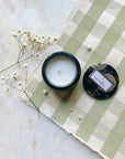 Moso Bamboo glass jar candle with tin lid off to the side, resting on green gingham paper with baby's breath to the side. 