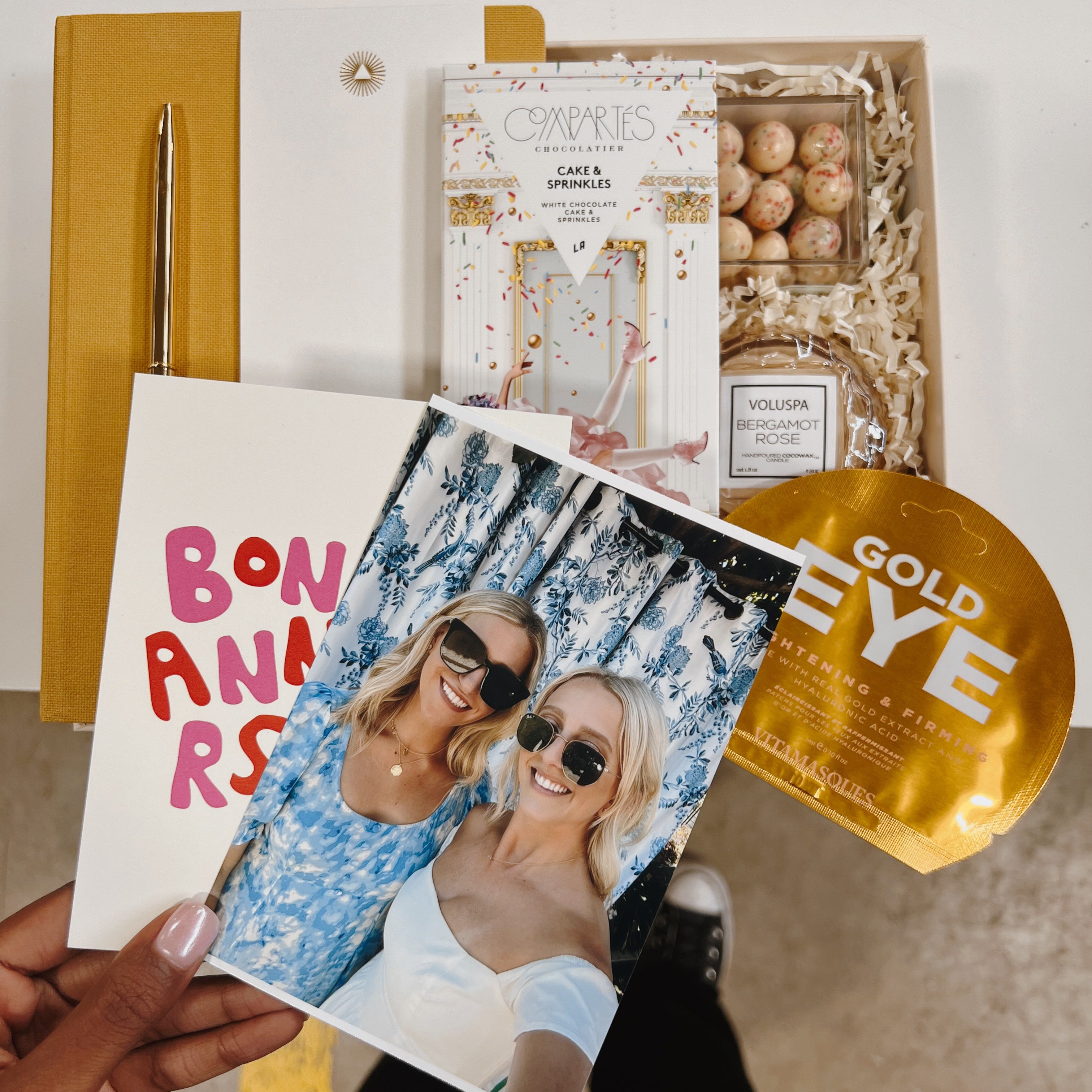 Birthday gift box with photo of two blonde girls and other card held in hand over gift box