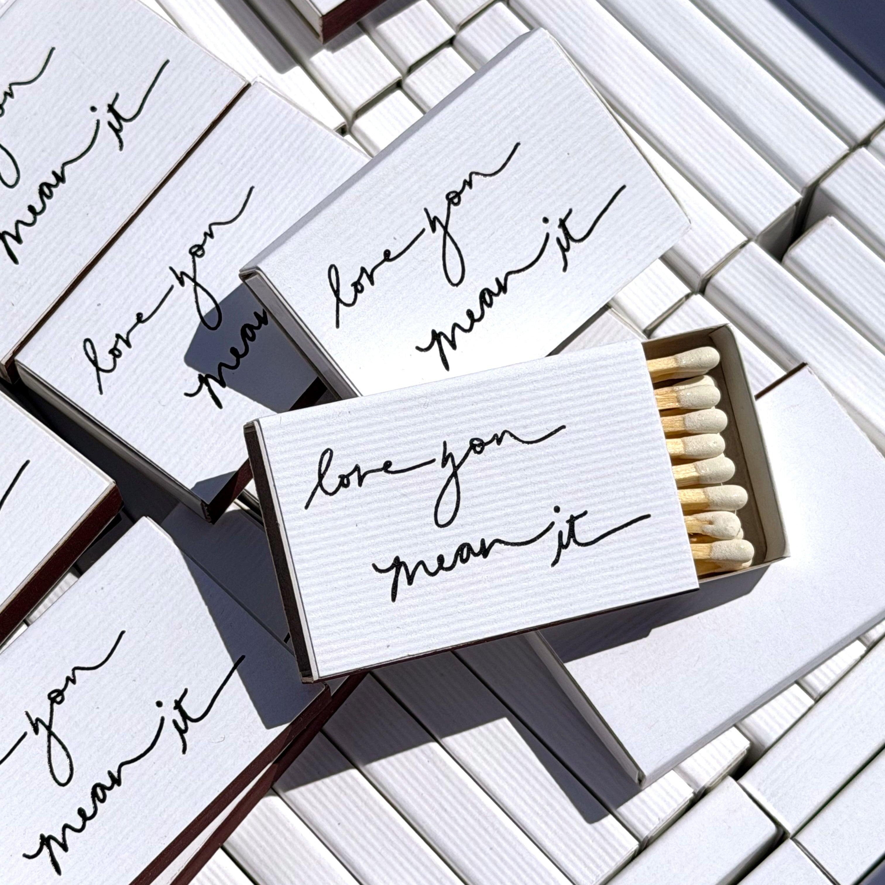 Matchboxes with 'love you mean it' text on a tiled surface