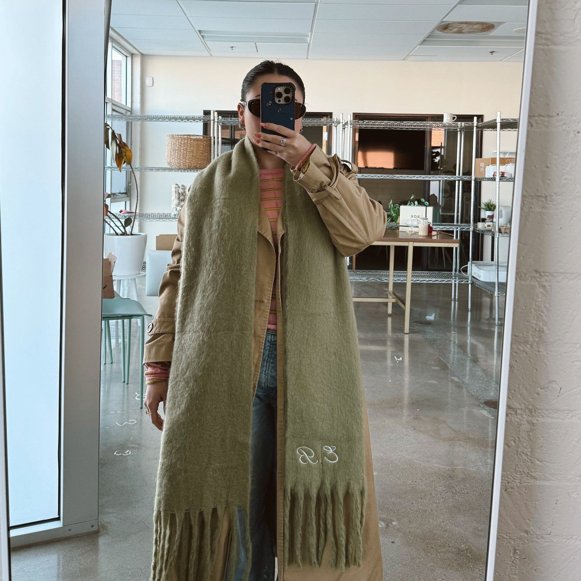 Person wearing a long green scarf with a brand logo in a room with large windows.