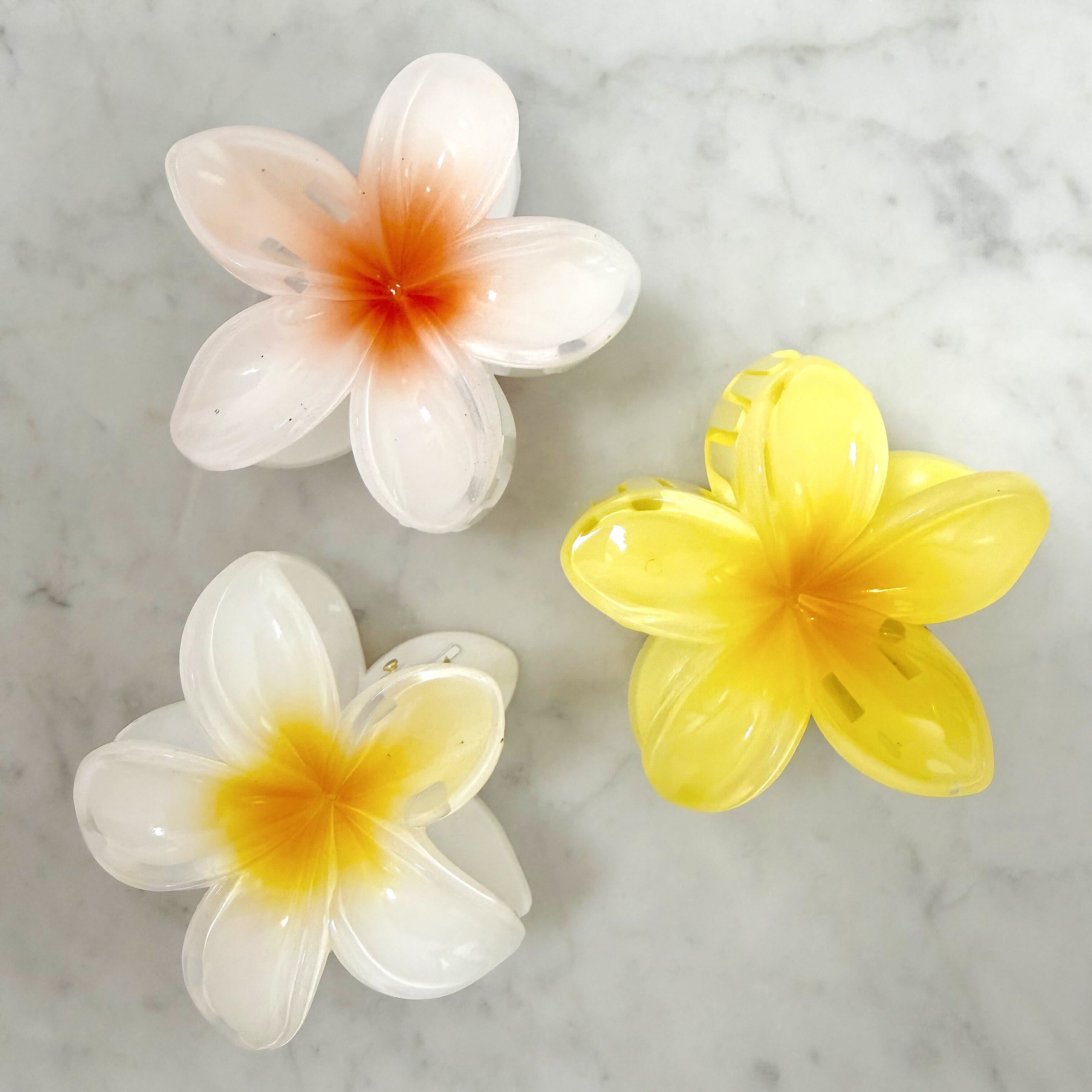 Three artificial flowers, two white and one yellow, on a marble surface.