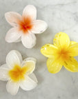 Three artificial flowers, two white and one yellow, on a marble surface.