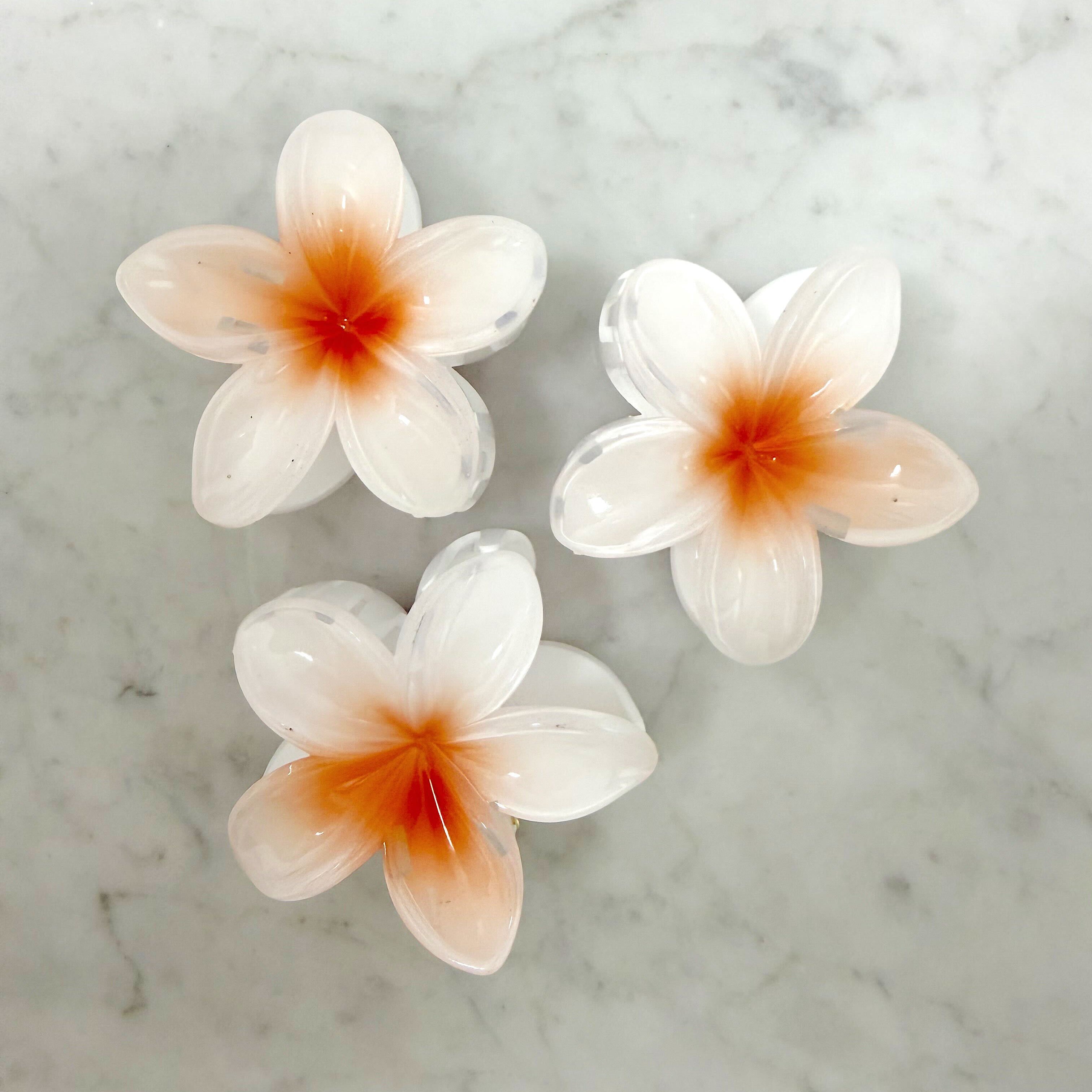 Three white flowers with orange centers on a marble surface