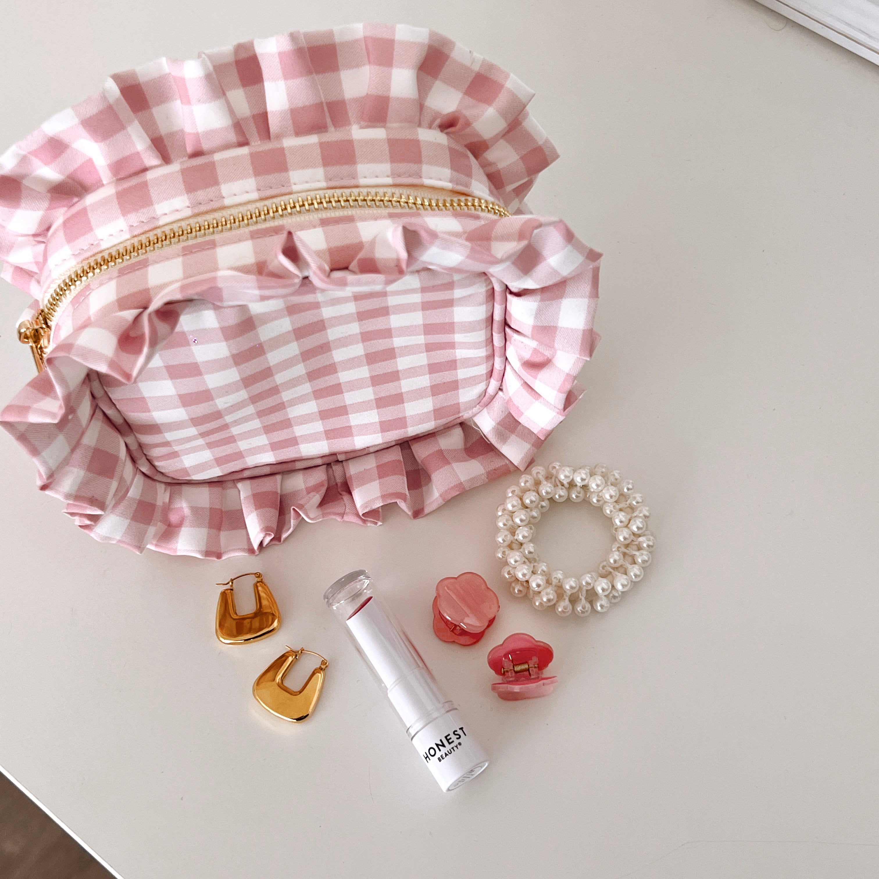 Pink Gingham Ruffle Pouch next to earrings, lipstick, hair clips and a scrunchie.