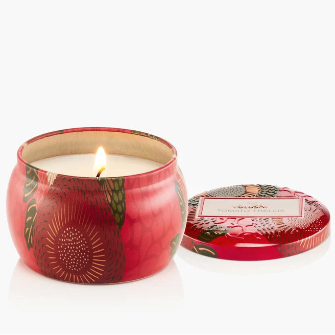 Candle in a decorative red tin with a floral design on a white background