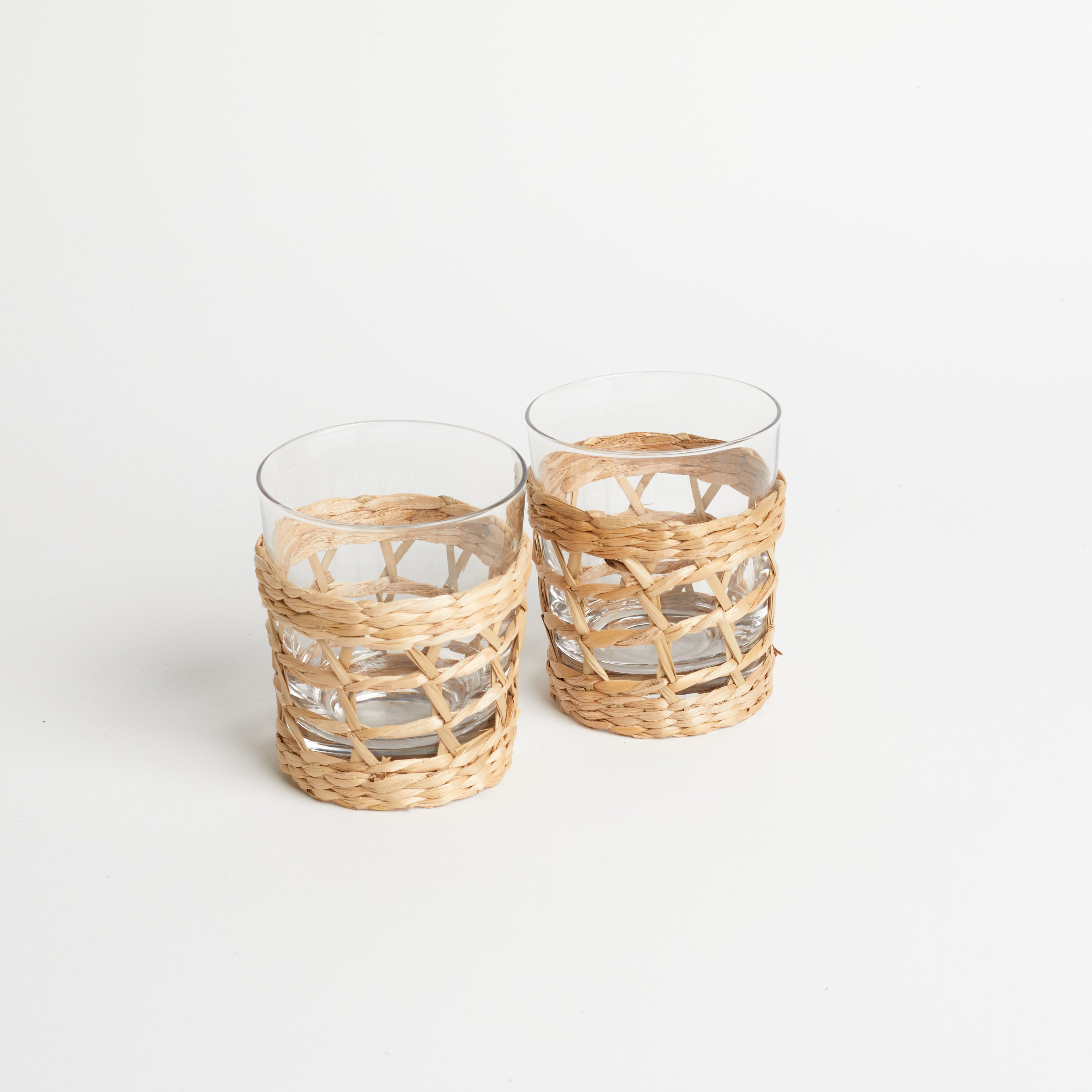Two seaglass cups wrapped in rattan sitting on a white table against a white background