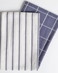 A blue and white plaid dish towel paired with a white and blue striped dish towel against a white background