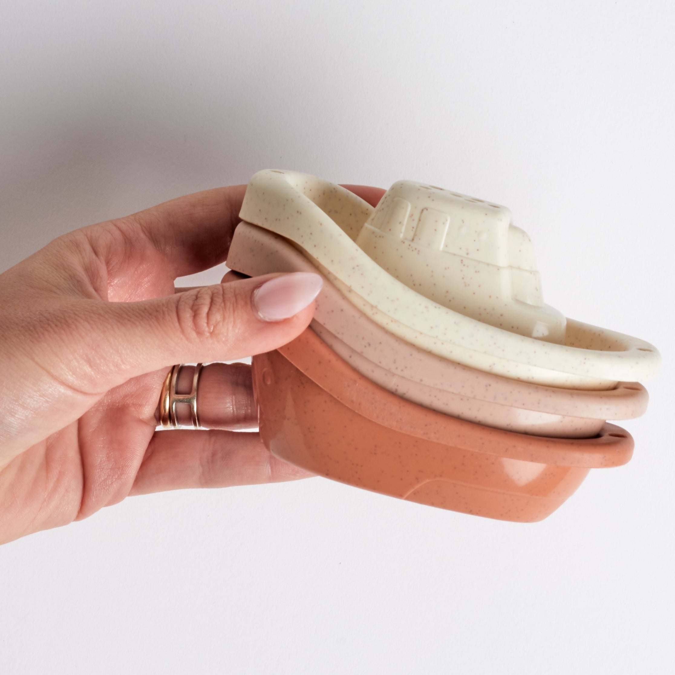 Hand holds stack of warm-toned stacking boat bath toys.