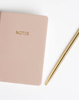 Pink leather notebook next to gold pen.