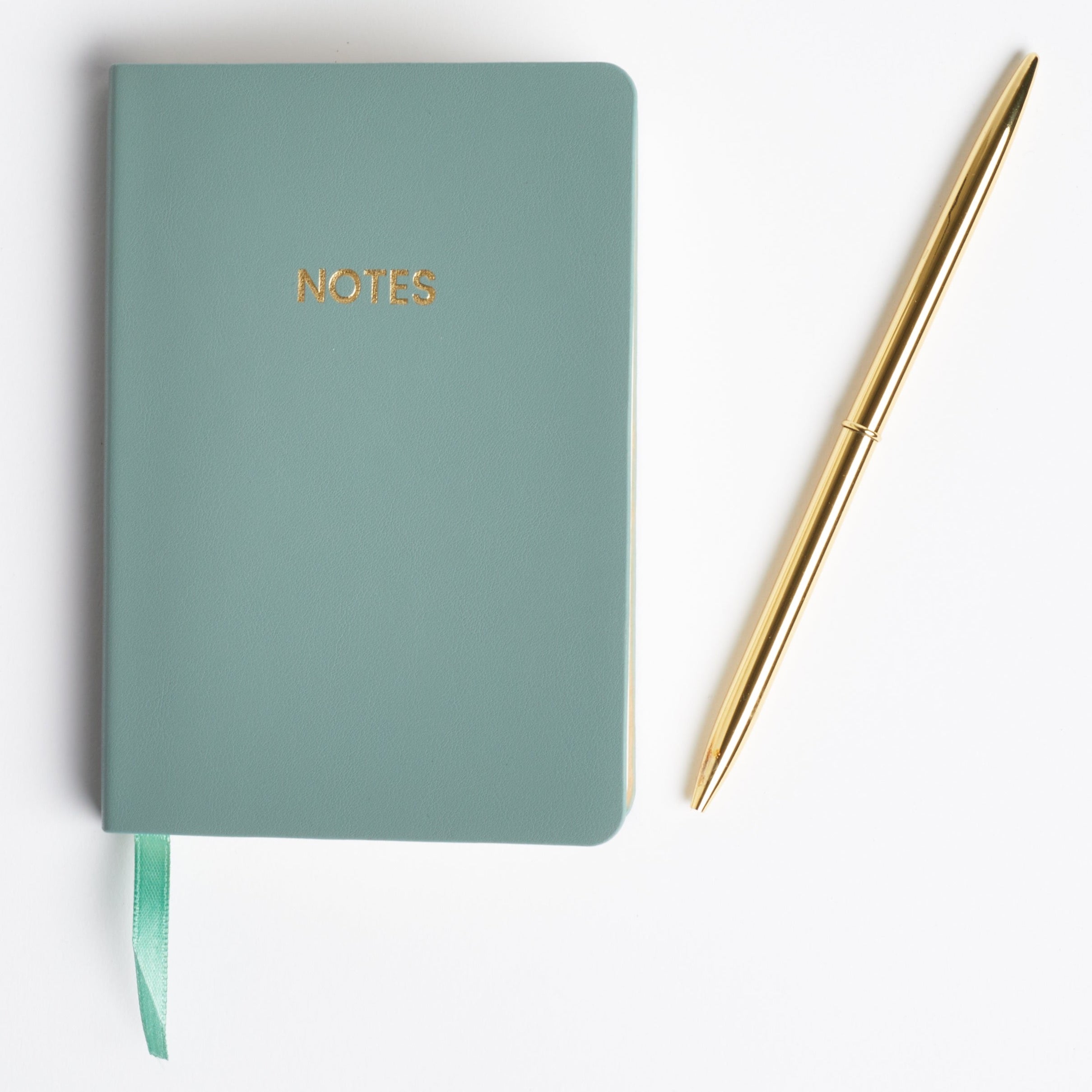 Sage green pocket-sized notebook with a gold "NOTES" written across the top. Next to a gold pen and against a white background