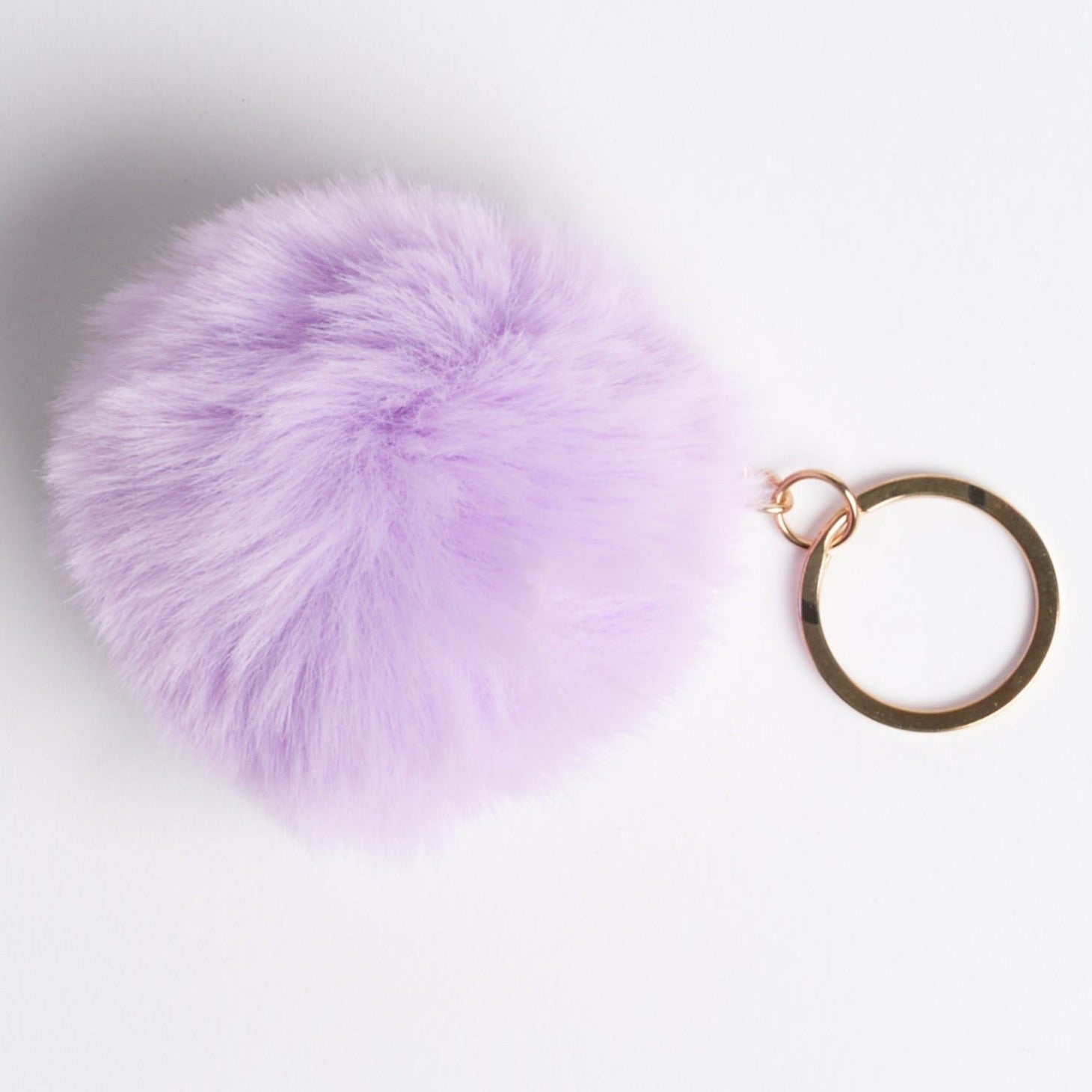 A lavender faux fur pom on a set of house keys. Photographed on a white background.
