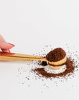 Gold Coffee Scoop + Clip with coffee grounds.