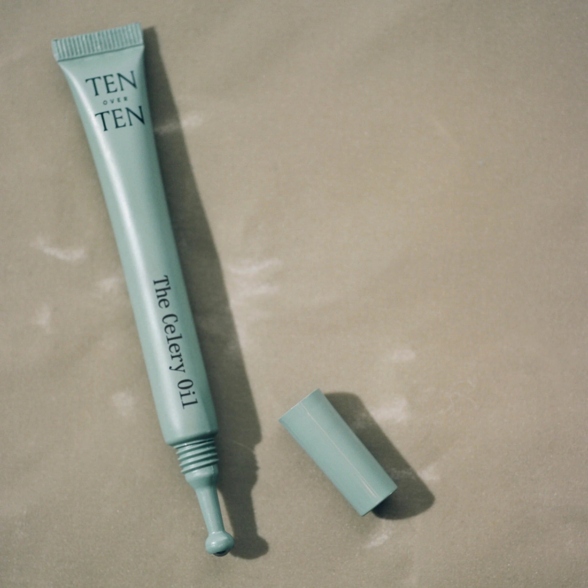 Teal skincare product tube labeled 'TEN' on a beige background