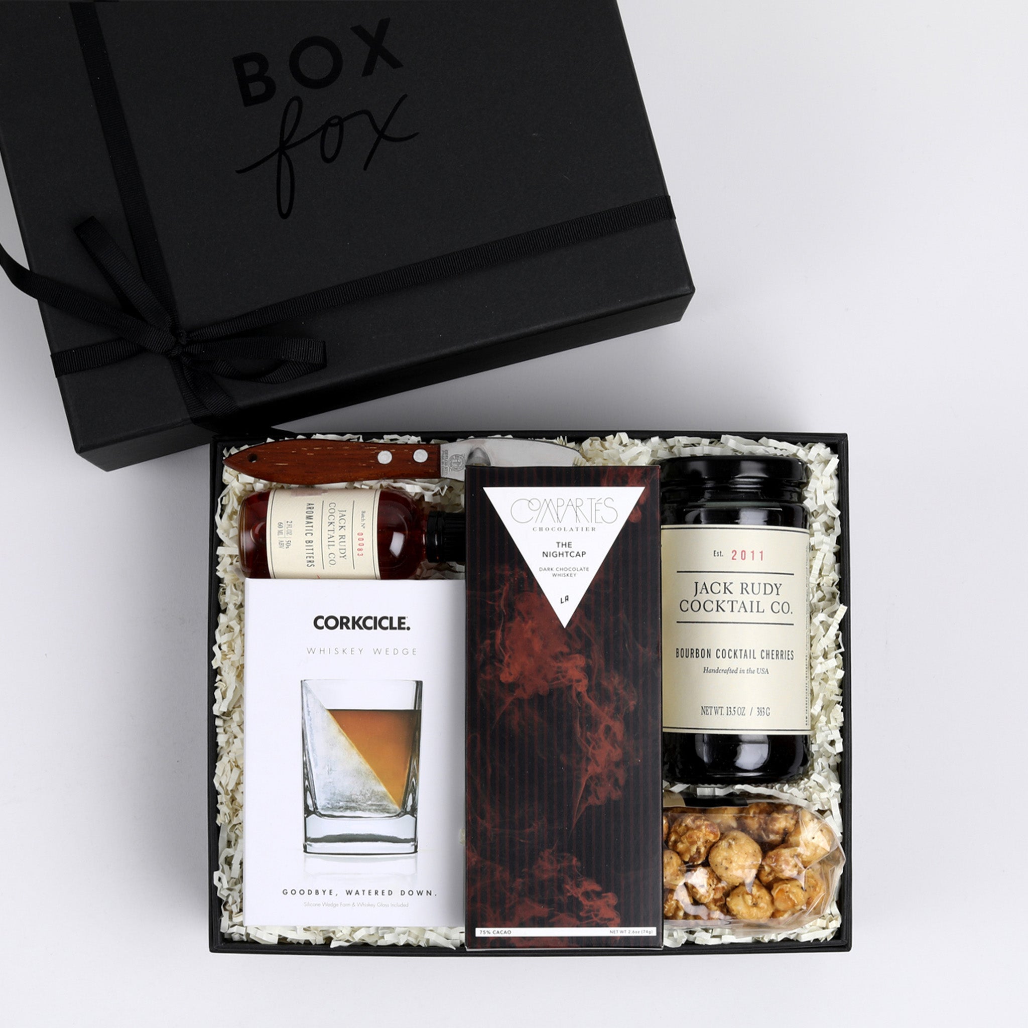 BOXFOX Matte Black Gift Box filled with Compartes The Nightcap Chocolate Bar, Corkcicle Whiskey Wedge Glass, Mielle Citrus Peeler, Art of Caramel Kentucky Bourbon Black Pepper Popcorn, Jack Rudy Cocktail Co. Aromatic Bitters and Jack Rudy Cocktail Co. Bourbon Cocktail Cherries