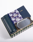 A gift set in a striped box containing a dark teal insulated bottle, a navy notebook with gold foil 'NOTES' text, a patterned purple notebook, and a stainless steel tray on a white background.