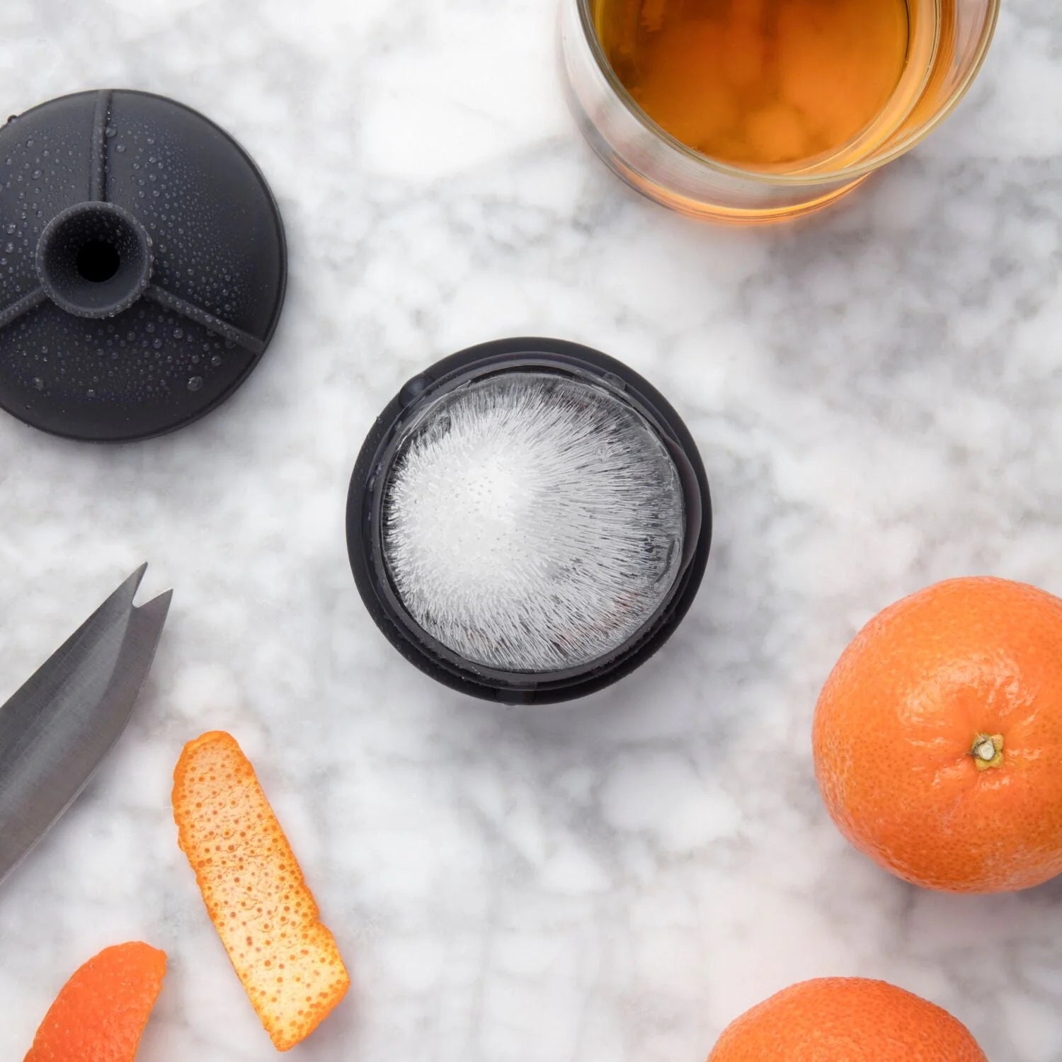 Charcoal Single Sphere Ice Mold with ice cube, surrounded by whiskey and orange slices