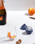 Charcoal Single Sphere Ice Mold surrounded by champagne bottle, orange, and glass