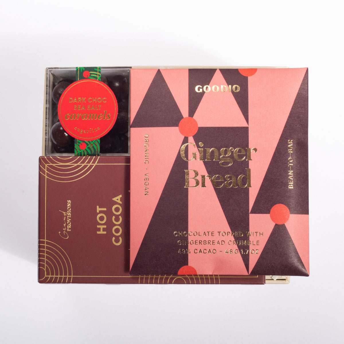 A boxed food product set on a white background, featuring a pink and dark brown geometric package labeled GOODINO Ginger Bread, alongside a smaller brown box labeled GOODINO Hot Cocoa and a round red sticker reading Dark Chocolate Candies.