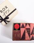 A gift box set from Goodies featuring a cream-colored 'Box fox' box with a black ribbon, alongside an open gift box containing chocolate gingerbread cookies, hot cocoa, and a small jar of caramel.