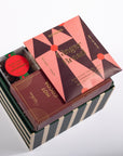 A gourmet gift box set containing a gingerbread cookie, a hot cocoa box, and a small caramel candy, presented in a striped box on a white background.