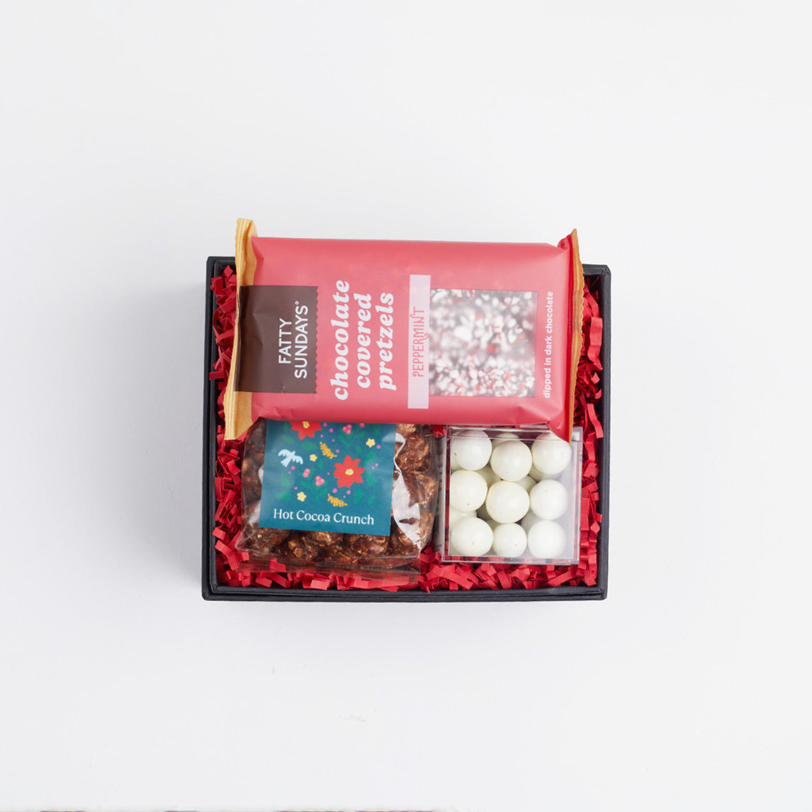 BOXFOX black gift box packed with red crinkle and peppermint chocolate pretzels, mini hot cocoa crunch popcorn and candy cane caramels.