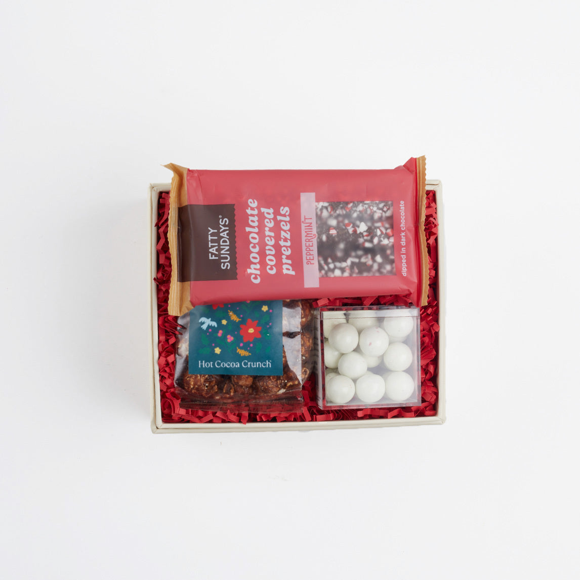 BOXFOX creme gift box packed with red crinkle and peppermint chocolate pretzels, mini hot cocoa crunch popcorn and candy cane caramels.