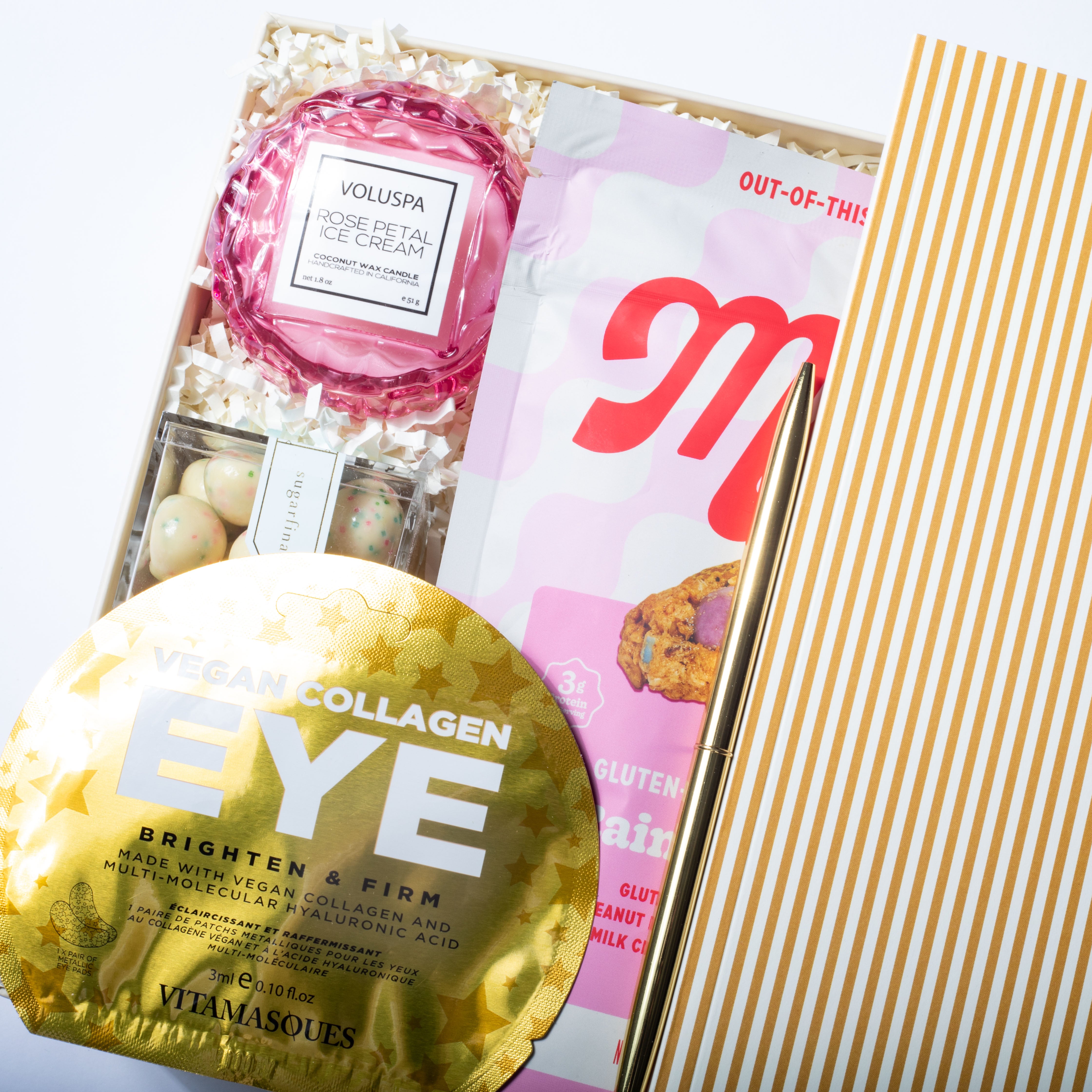 Collagen eye mask, Voluspa product, and a magazine on a white surface with a gold and white striped background.