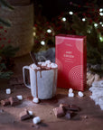Hot chocolate with marshmallows, a box of hot cocoa mix, and Christmas decorations.