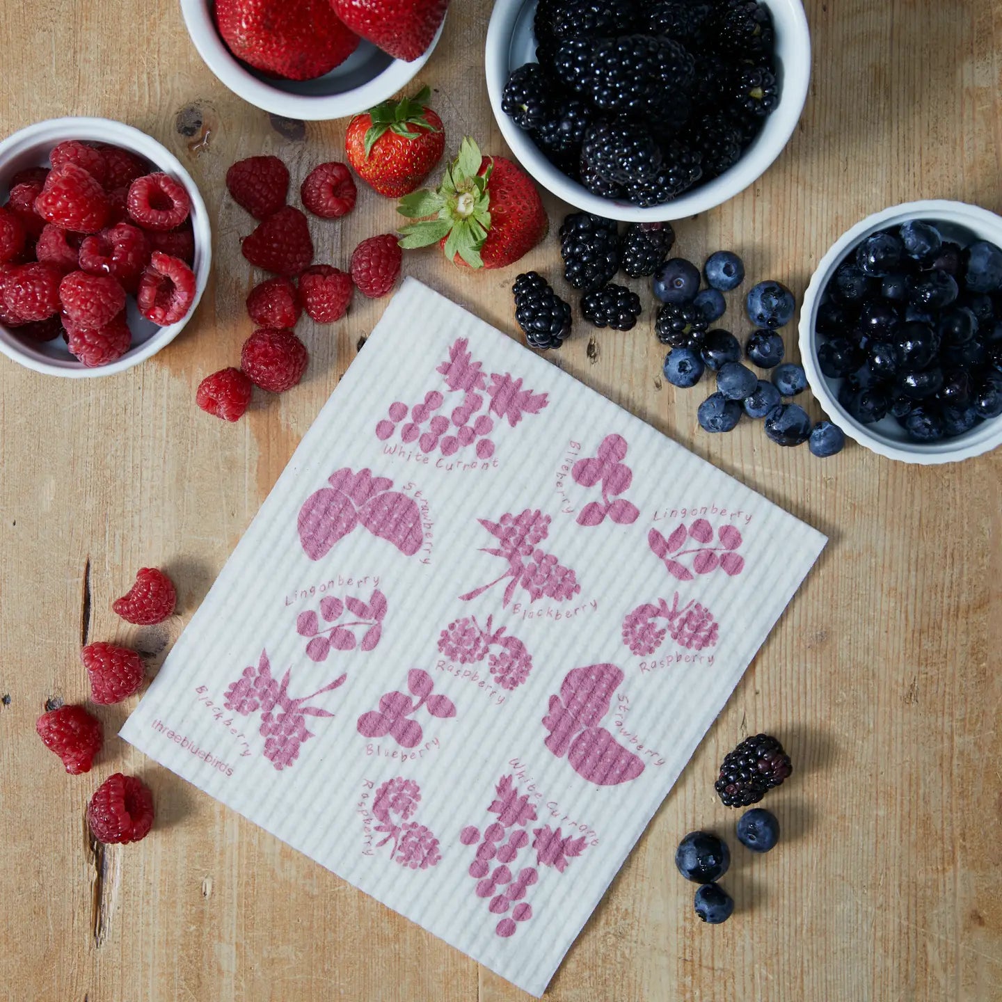 Dishcloth with berry pattern on a wooden surface with bowls of berries