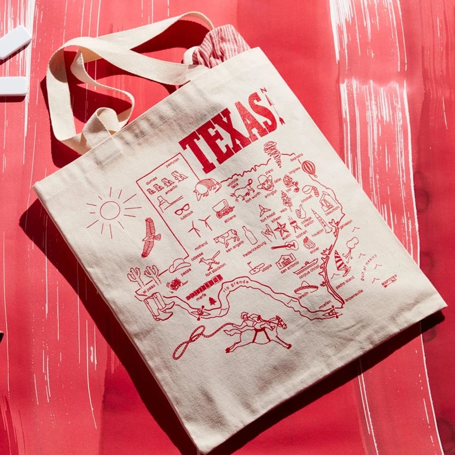 texas tote on red table. tote Is canvas with red illustrated map of Texas and illustrations for each city