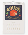 June page of the 2025 Cheese Calendar featuring Gouda cheese from South Holland. The page includes an illustration of a cheese wheel with a Dutch flag and floral decorations on a dark background