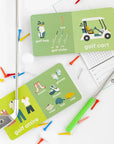 open golf baby books surrounded by golf clubs, tees, and balls