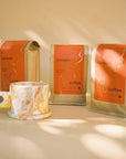 A collection of three Canyon Coffee Holiday Blend bags displayed upright with a colorful, speckled ceramic mug beside them. The background is softly lit, adding a cozy and artistic vibe.

