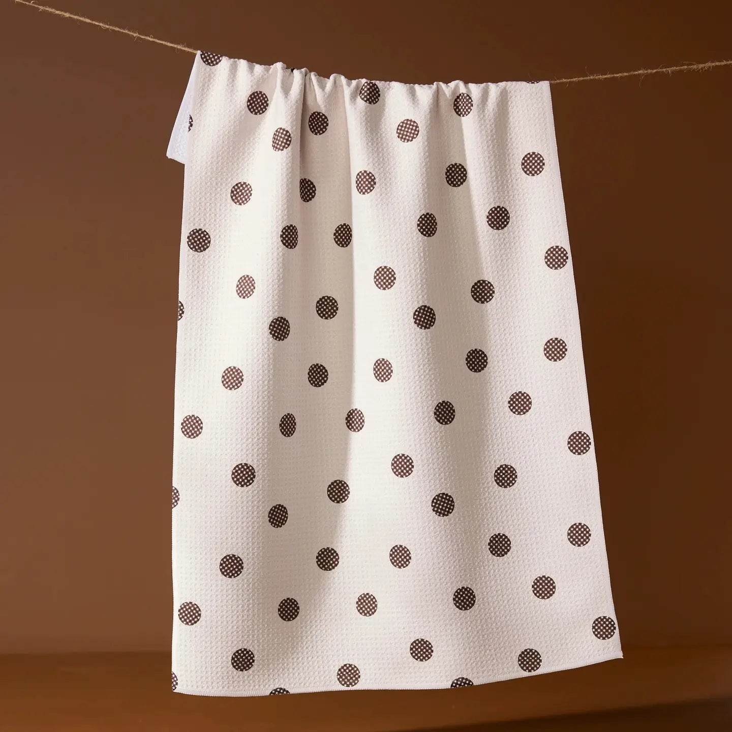 White towel with brown polka dots hanging on a line against a brown background
