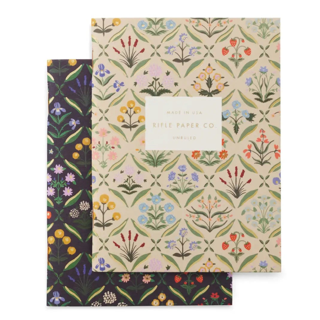Two small notebooks stacked on top of each other. Notebooks have a flower print on them. One has a black background &amp; one has a beige background
