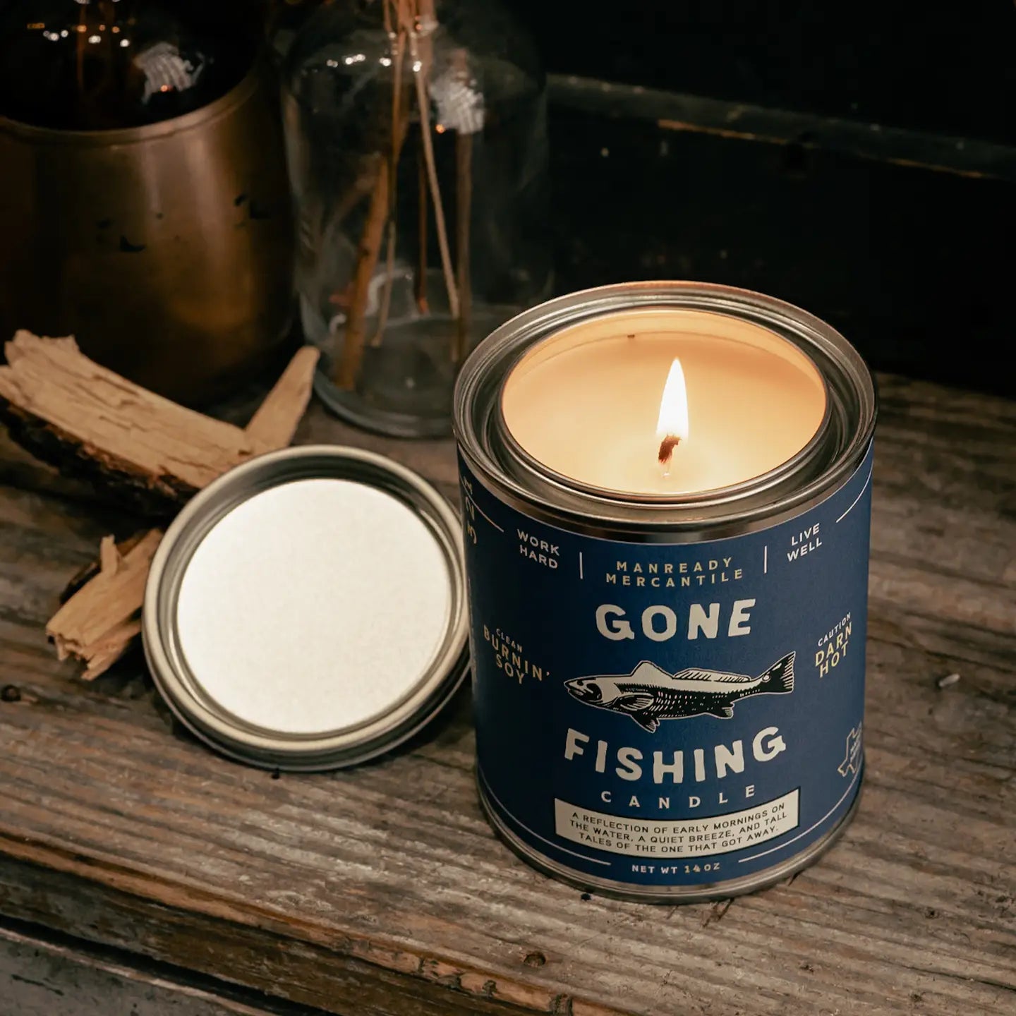 Candle in a 'Gone Fishing' can on a wooden surface with natural light.