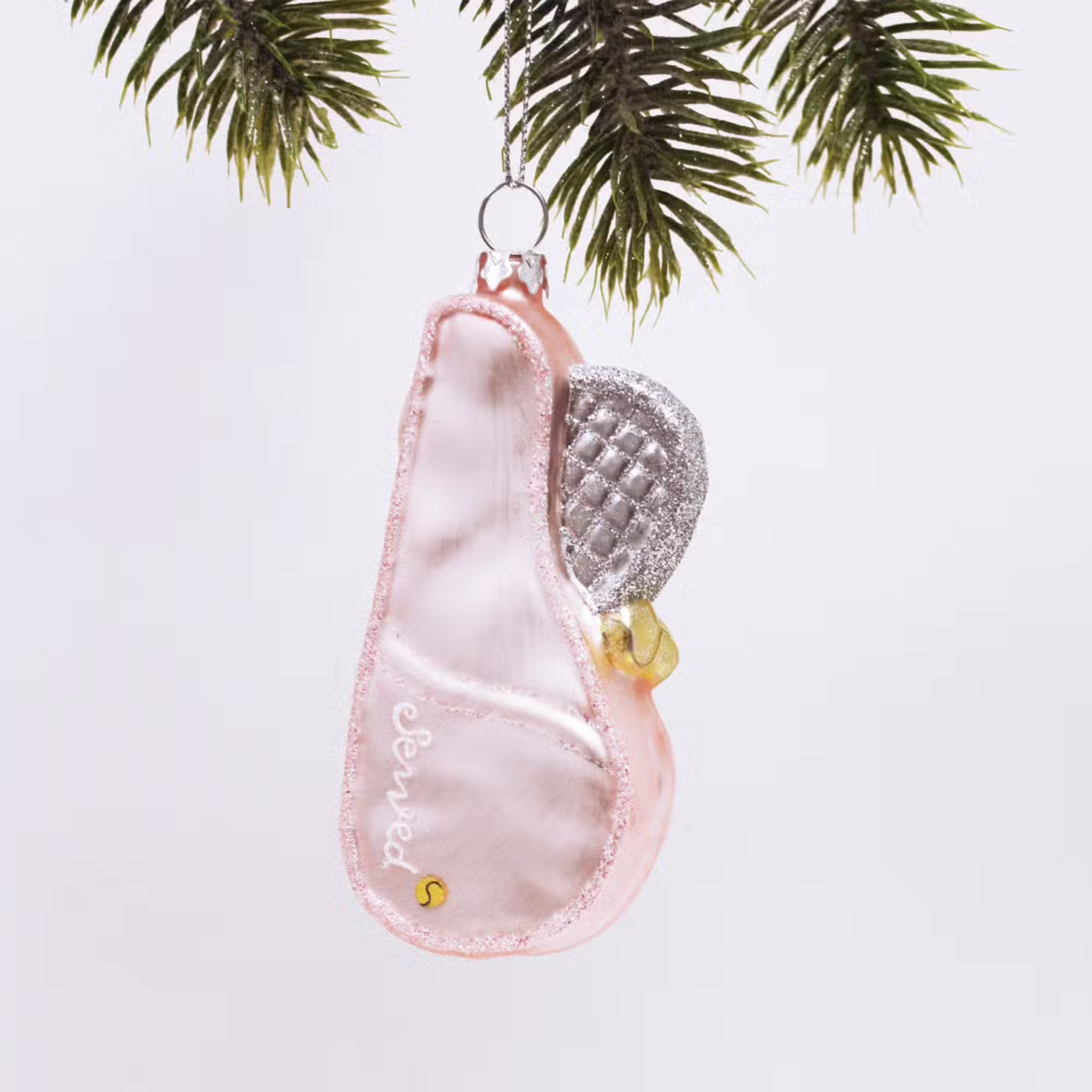 pink tennis racket bag shaped ornament with a silver and glittery racket sticking out of the bag. Ornament is hanging from tree.