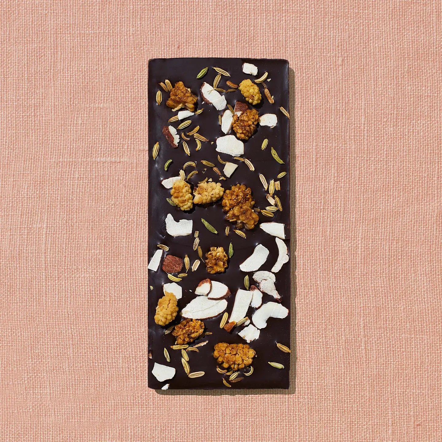 Dark chocolate bar with various toppings on a pink textured background