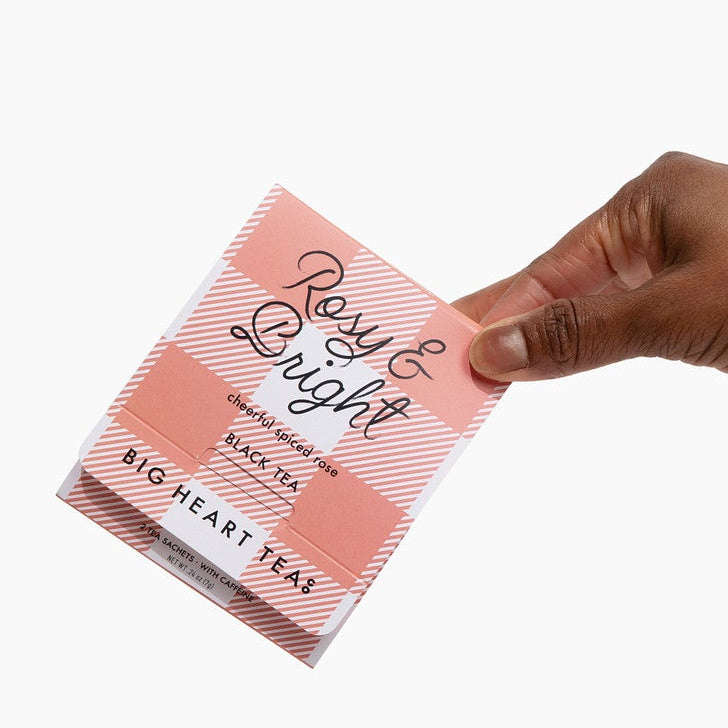 Hand holding a pink box of tea against a white background