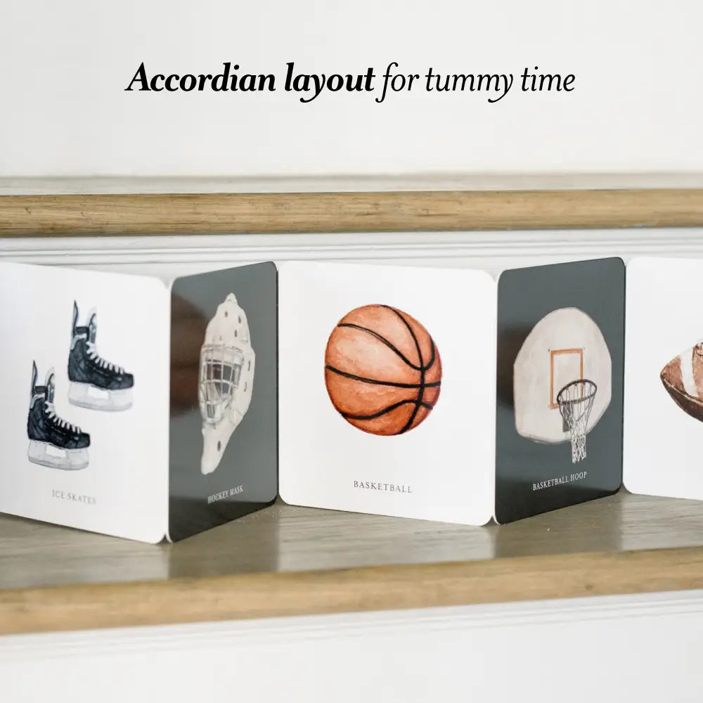 Accordian layout book for tummy time with sports-themed illustrations on a wooden surface.