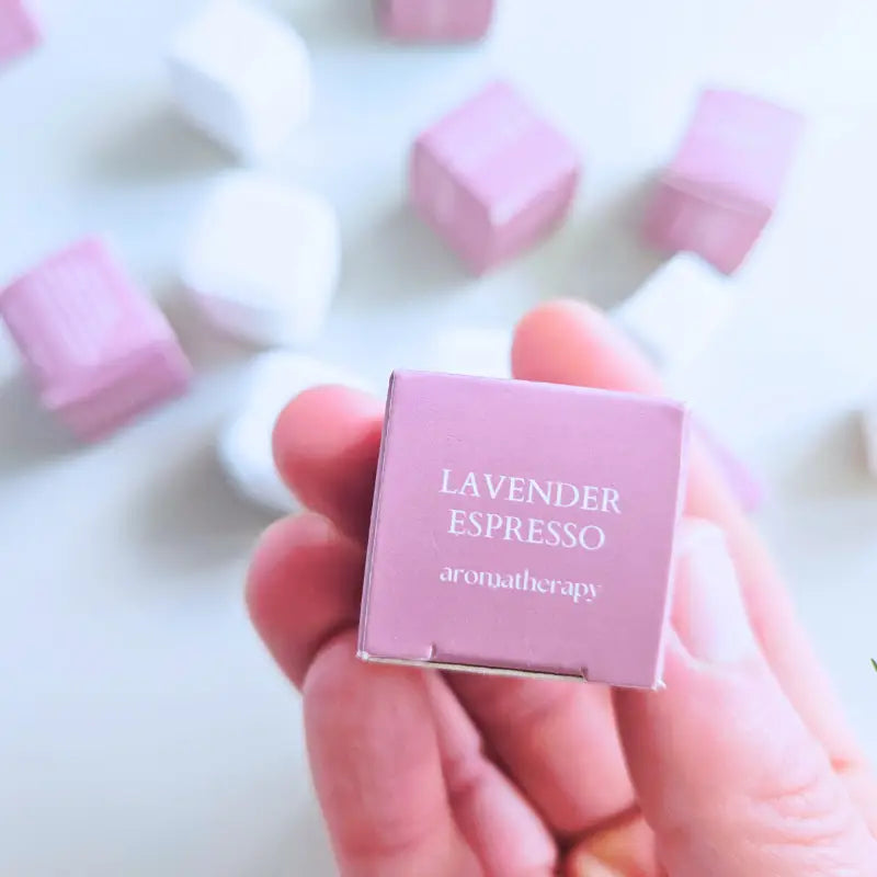 Pink box labeled 'Lavender Espresso' held by a hand with blurred pink and white background