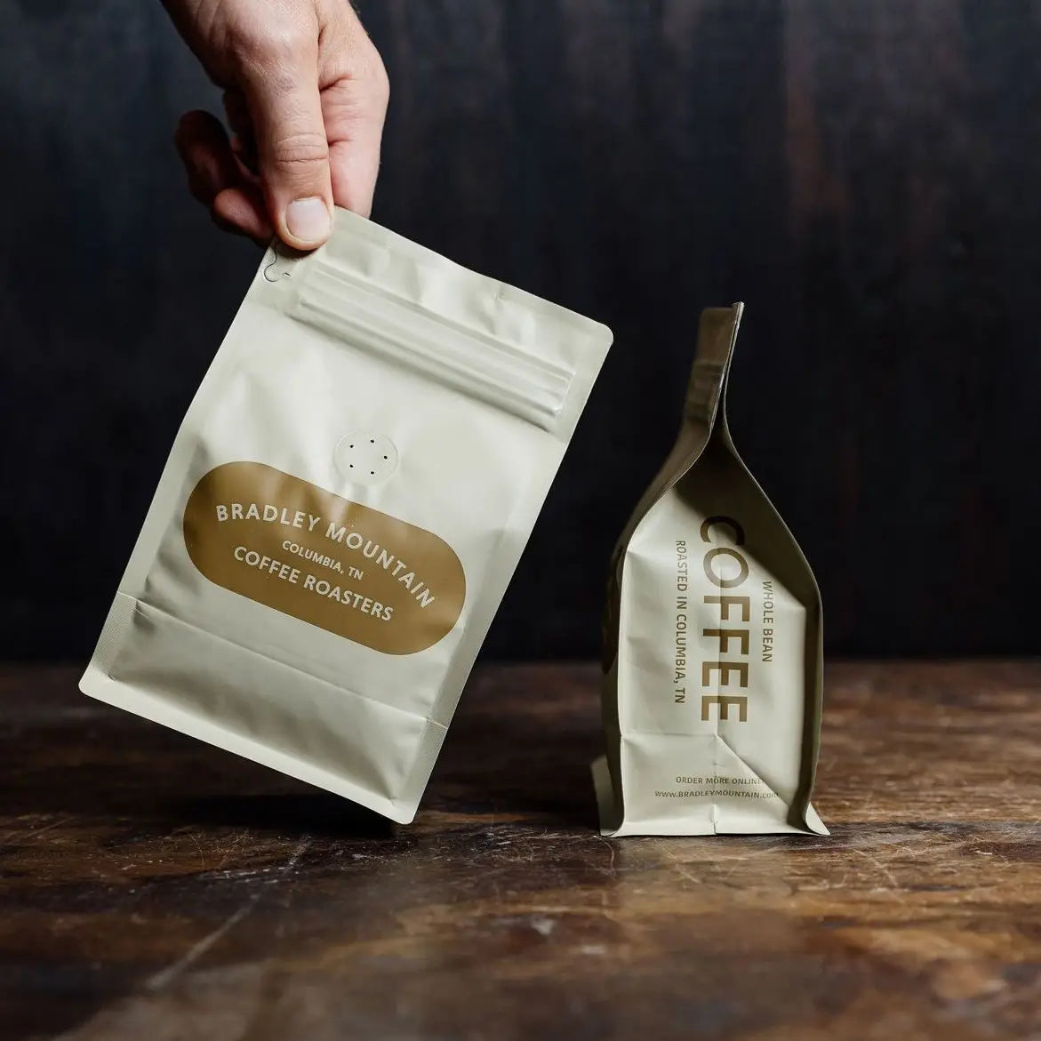 Hand holding a coffee package with 'Bradley Mountain Coffee Roasters' branding on a wooden surface.