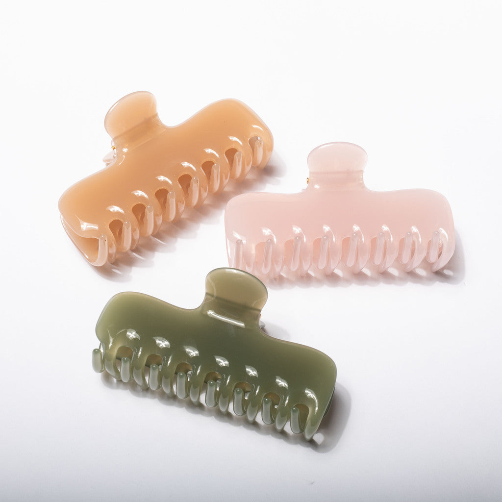 Three translucent hair claw clips in peach, pale pink, and sage green, arranged diagonally on a clean white background.